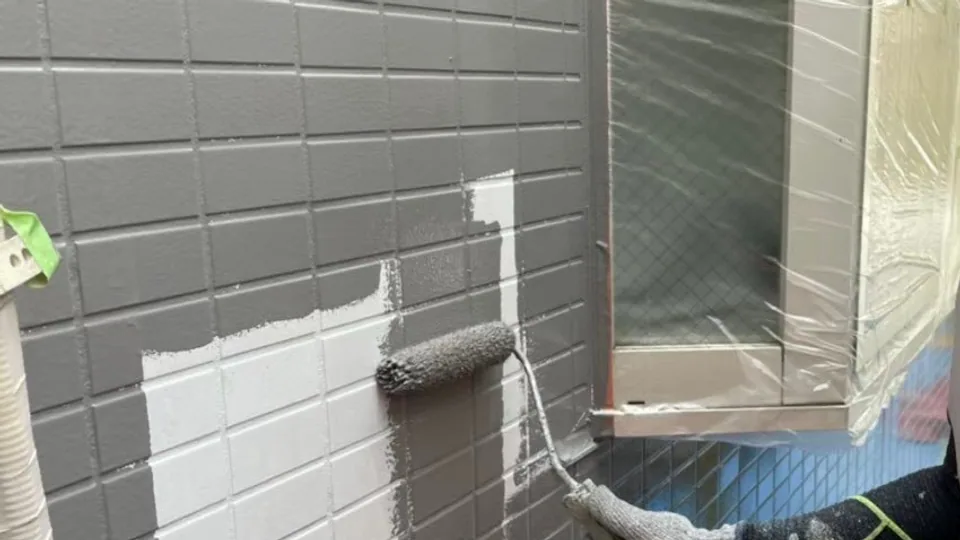 養生した窓のそばでローラーを使い外壁を塗装するヒイラギ建装の施工現場
